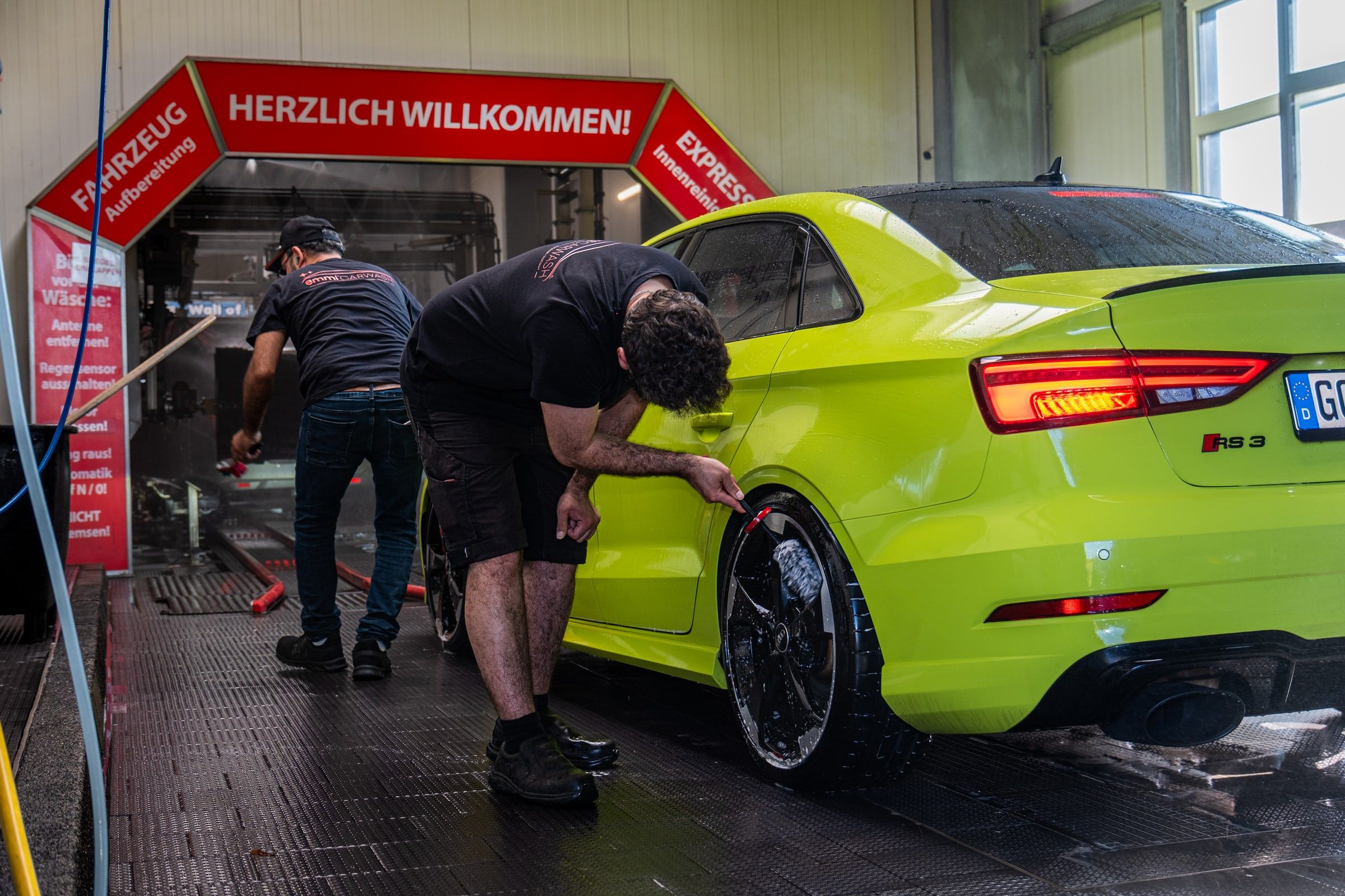 Das Team von emmi Carwash wäscht ein Auto von Hand vor der Einfahrt in die Waschstraße