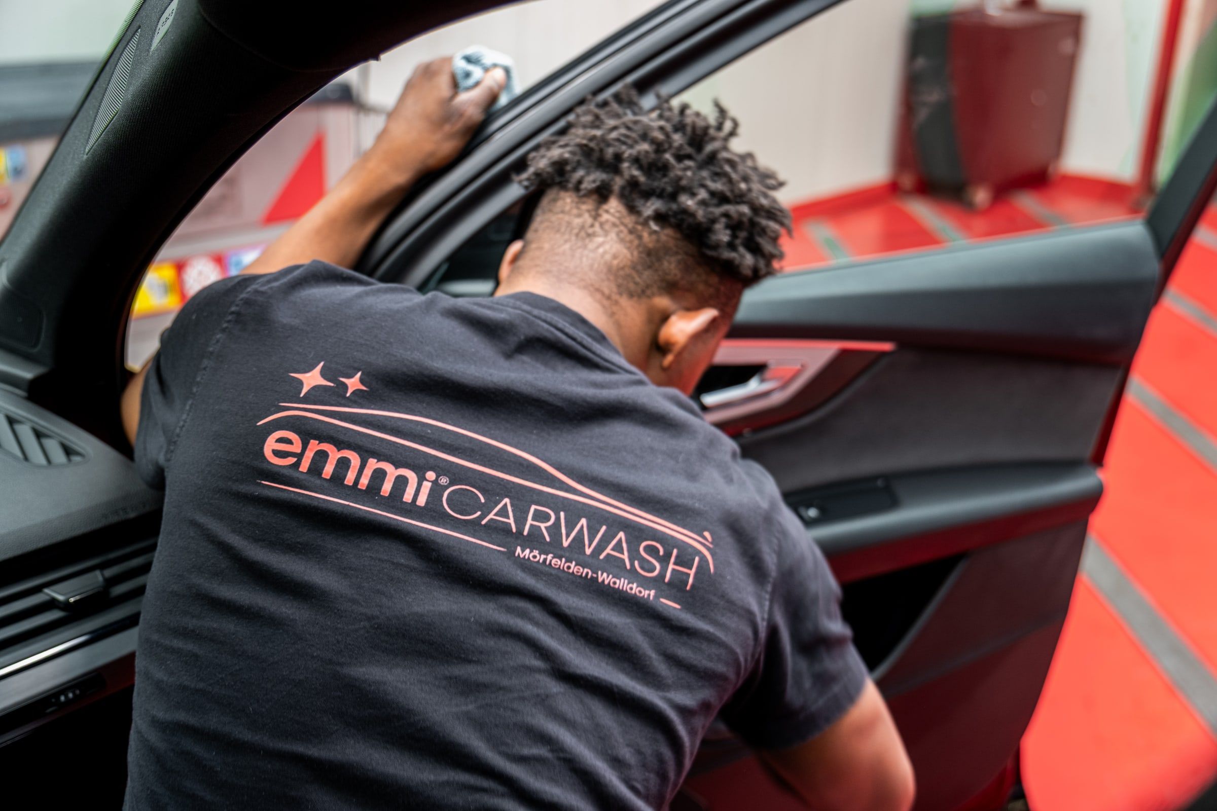 Mitarbeiter von emmi Carwash reinigt die Türverkleidung eines Autos von Hand