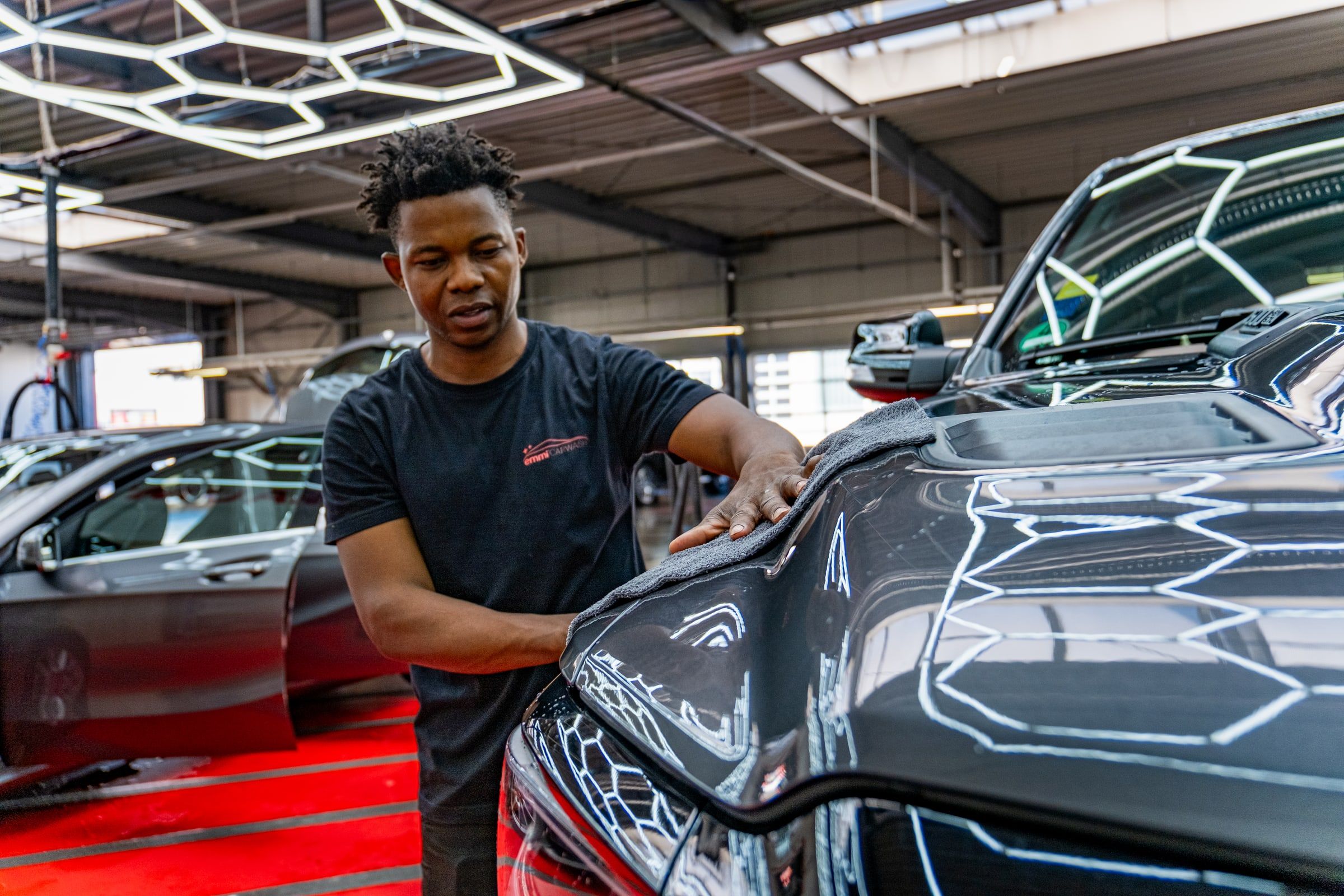 Mitarbeiter von emmi Carwash trocknet eine Motorhaube von Hand